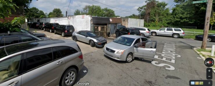 Google Maps “Street View” image looking Northwest down South Edgewood toward the L-shaped intersection with Trinity Street, showing Defendants’ property and the opening of the shared alleyway dominated by Defendants’ operations and illegal vehicle storage. Photo taken July 2021.